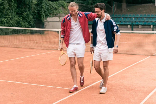 Cheerful Sportive Friends Wooden Rackets Hugging Walking Tennis Court — стоковое фото